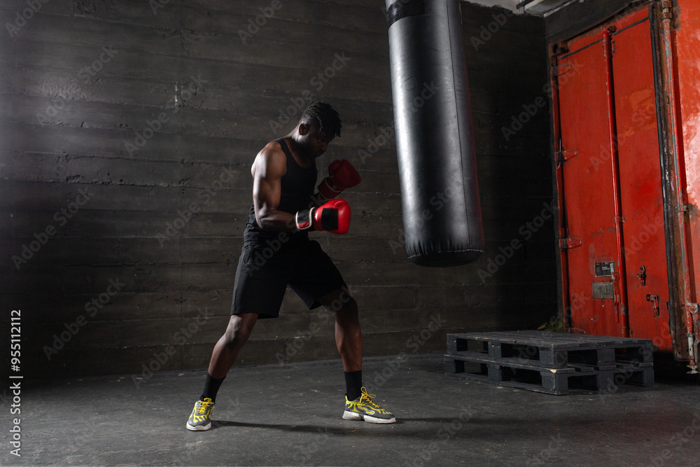 Powerful African American boxer wearing red gloves prepares to hit punching bag in gym showing his determination and strength, athlete trains before boxing competition Powerful African American boxer wearing red gloves prepares to hit punching bag in gym showing his determination and strength, athlete trains before boxing competition