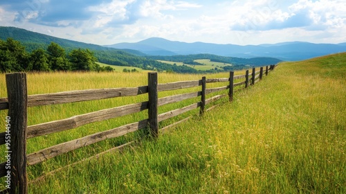 A rustic wooden fence dividing a field of tall grass from a scenic countryside, with rolling hills and distant mountains in the background.