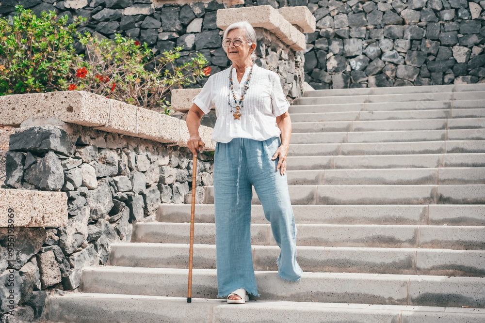 Smiling 70 year old elderly woman with walking disability holding stick knob while walking down stairs outdoors, leaning on stick, suffering from muscle problems, bone disease, recovering from trauma Smiling 70 year old elderly woman with walking disability holding stick knob while walking down stairs outdoors, leaning on stick, suffering from muscle problems, bone disease, recovering from trauma