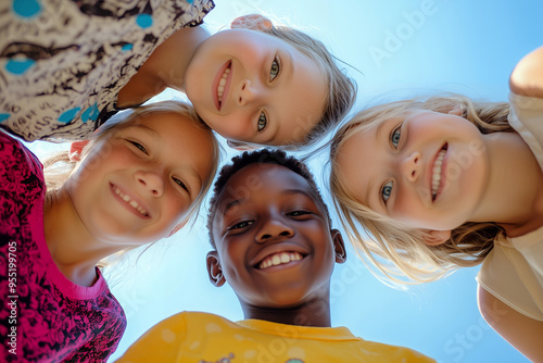 Bunch of cheerful joyful cute little children playing together and having fun. Group portrait of happy kids huddling, looking down at camera and smiling. Low angle, view from below. Friendship concept