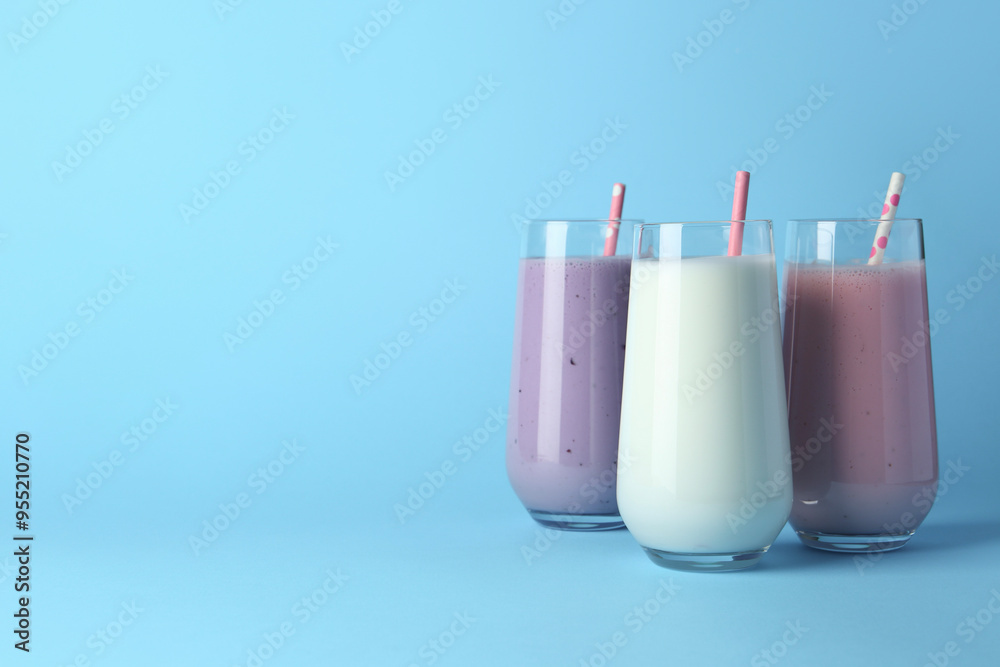 Different tasty yogurts and straws in glasses on light blue background, space for text Different tasty yogurts and straws in glasses on light blue background, space for text