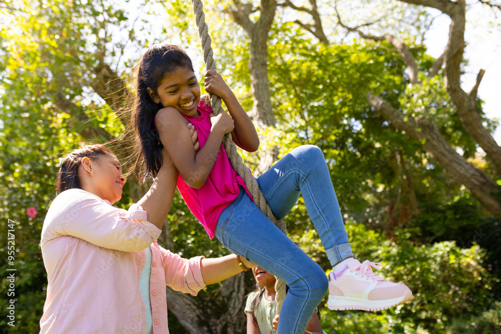 Mother helping daughter swing on rope in backyard, enjoying family time outdoors Mother helping daughter swing on rope in backyard, enjoying family time outdoors