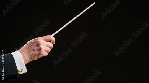 A close-up of a conductor's hand holding a baton against a dark background, symbolizing music and direction in performance.