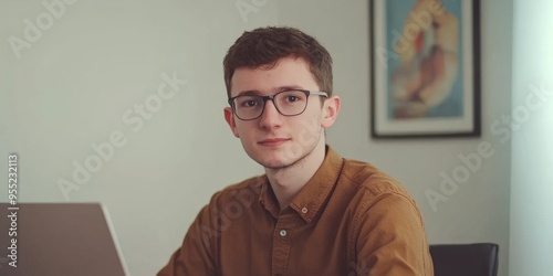 Dedicated Young Programmer: Portrait of Focused Male Developer in Brown Shirt and Glasses Working on Laptop in Modern Office. Illustrating Tech Innovation, Work Culture, and Professional Dedication fo photo