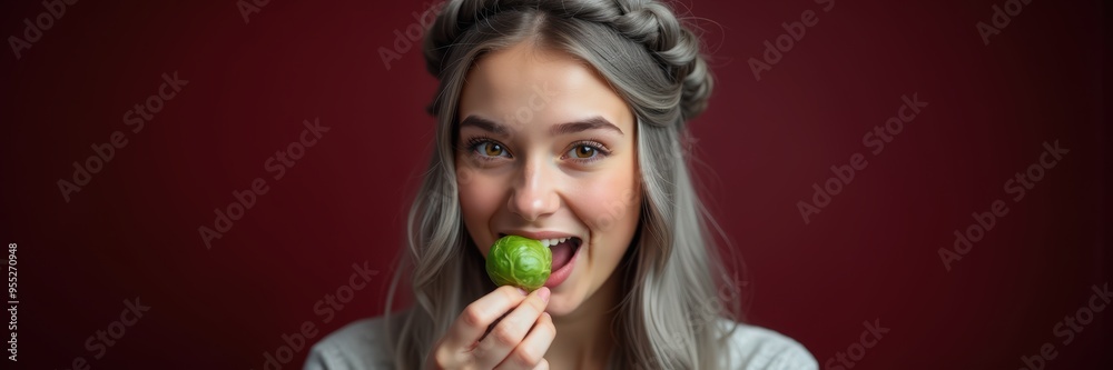 A young woman joyfully tasting a green dessert against a rich red background, embodying delight and indulgence in food. A young woman joyfully tasting a green dessert against a rich red background, embodying delight and indulgence in food.