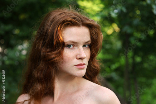 Portrait of ginger girl with long red hair and freckles in park. Young sensual model with naked shoulders, natural female beauty