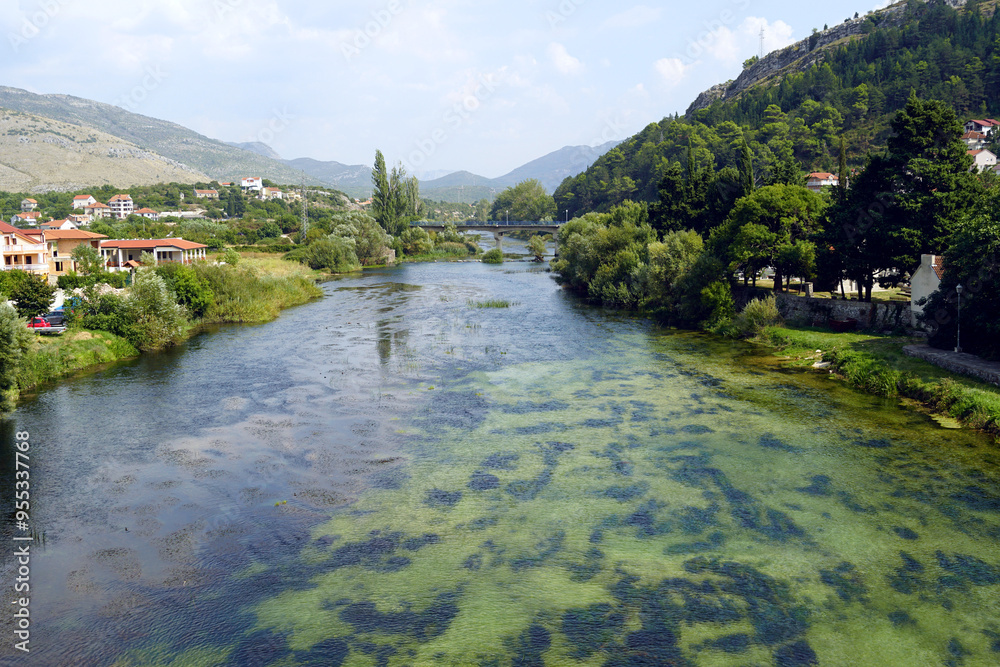 Fototapeta premium Landscape from Trebinje: view from the Arslanagic bridge to the Trebišnjica river, its green banks and mountains. Photo taken during a summer trip to the beautiful places of Bosnia and Herzegovina