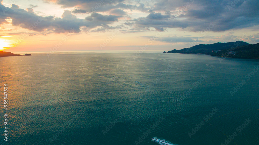 A breathtaking aerial view of a coastal bay at sunset, with golden light reflecting on the calm sea and silhouetted hills in the distance. beautiful reflection of the golden sun at Patong Bay Phuket. A breathtaking aerial view of a coastal bay at sunset, with golden light reflecting on the calm sea and silhouetted hills in the distance. beautiful reflection of the golden sun at Patong Bay Phuket.