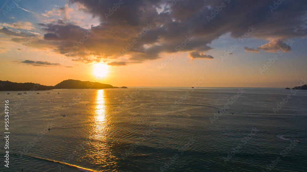 A breathtaking aerial view of a coastal bay at sunset, with golden light reflecting on the calm sea and silhouetted hills in the distance. beautiful reflection of the golden sun at Patong Bay Phuket. A breathtaking aerial view of a coastal bay at sunset, with golden light reflecting on the calm sea and silhouetted hills in the distance. beautiful reflection of the golden sun at Patong Bay Phuket.