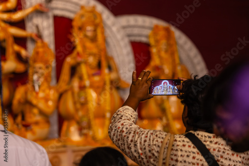 Photography Hand holding mobile phone and taking photos of Goddess Durga idol at a pandal
