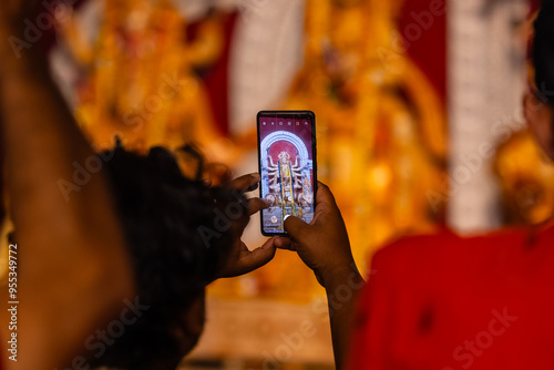 Photography Hand holding mobile phone and taking photos of Goddess Durga idol at a pandal