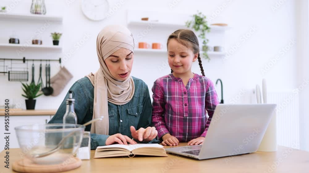 Cozy and educational moment focused on family, cooking, and technology. Muslim mother and daughter sitting at kitchen table and buying ingredients for meal using laptop, bank card and recipe book. Cozy and educational moment focused on family, cooking, and technology. Muslim mother and daughter sitting at kitchen table and buying ingredients for meal using laptop, bank card and recipe book.