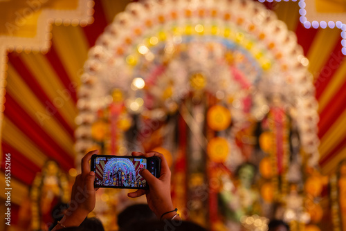 Photography Hand holding mobile phone and taking photos of Goddess Durga idol at a pandal