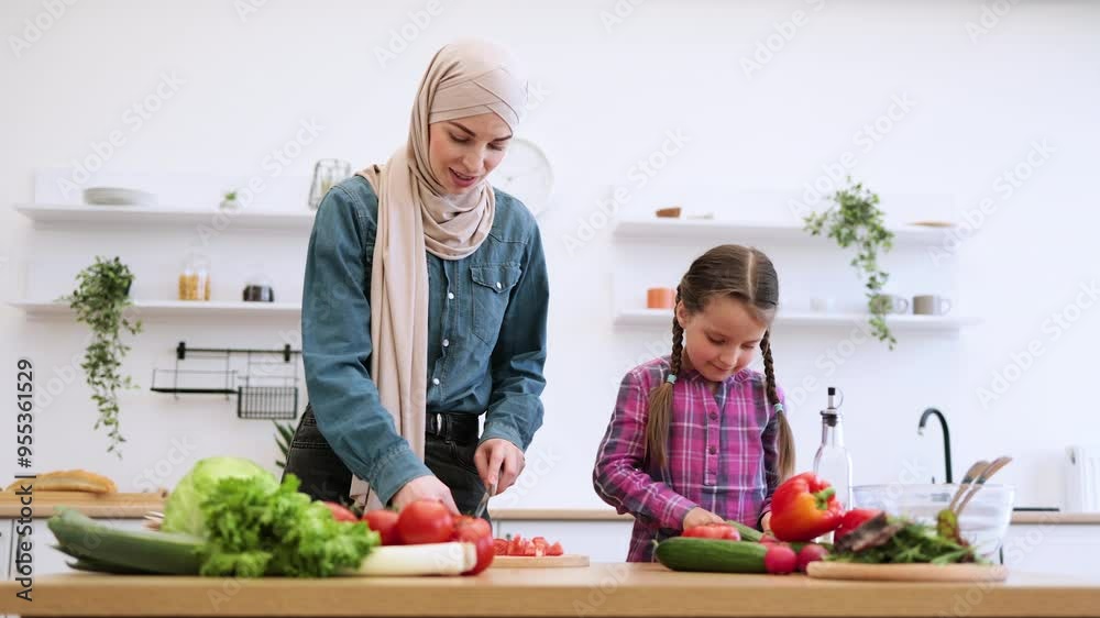 Fresh vegetables on wooden counters create healthy and joyful cooking environment. Muslim mother and daughter cutting ingredients for salad in modern kitchen.