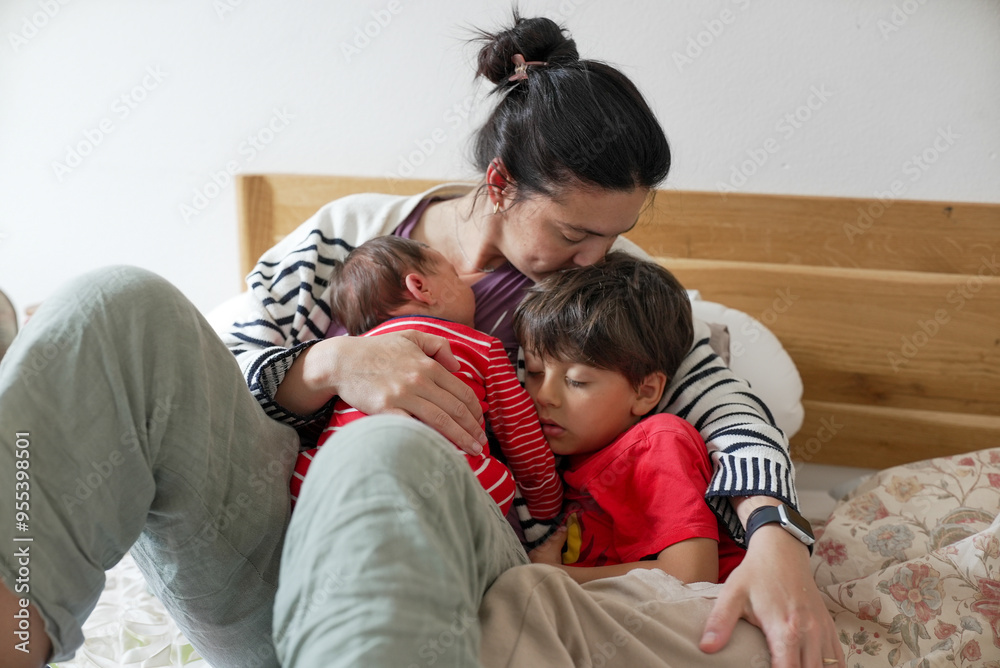 Mother cuddling her two children, one newborn and one young boy, both peacefully sleeping on a bed, showcasing family love and bonding Mother cuddling her two children, one newborn and one young boy, both peacefully sleeping on a bed, showcasing family love and bonding