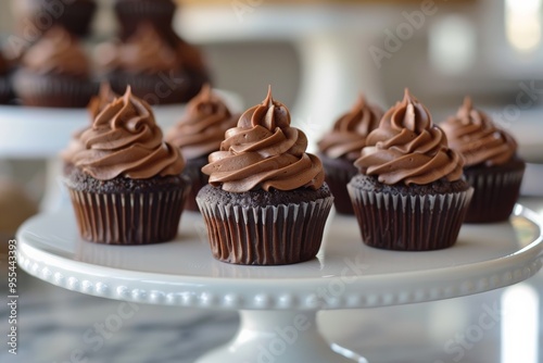 Decadent chocolate cupcakes with swirls of creamy chocolate frosting, beautifully displayed on a white cake stand in a cozy kitchen setting.