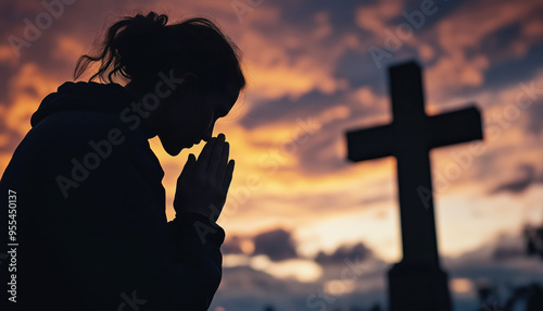 Woman praying on her knees, christian cross in background. Only silhouette visible against sunset coloured sky. Generative AI