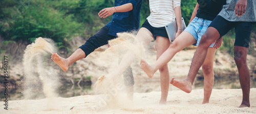 Fotografi Group of legs of friends play, and kick sand together while enjoying at beach, Casual clothing and barefooted fun highlight the carefree and joyful at beach outing-friendship concept