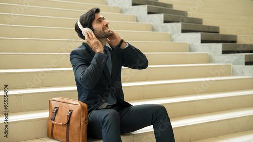 Professional business man picking and listening music by using headphone while sitting at stairs. Project manager dance while listening song while wearing headphone, suit. White background. Exultant.