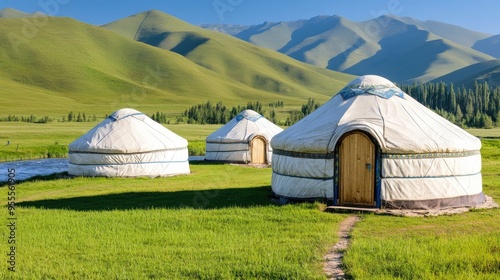 Aerial view of traditional yurts situated in vibrant green grass and forests, offering stunning vistas along the riverbanks in a mountainous region