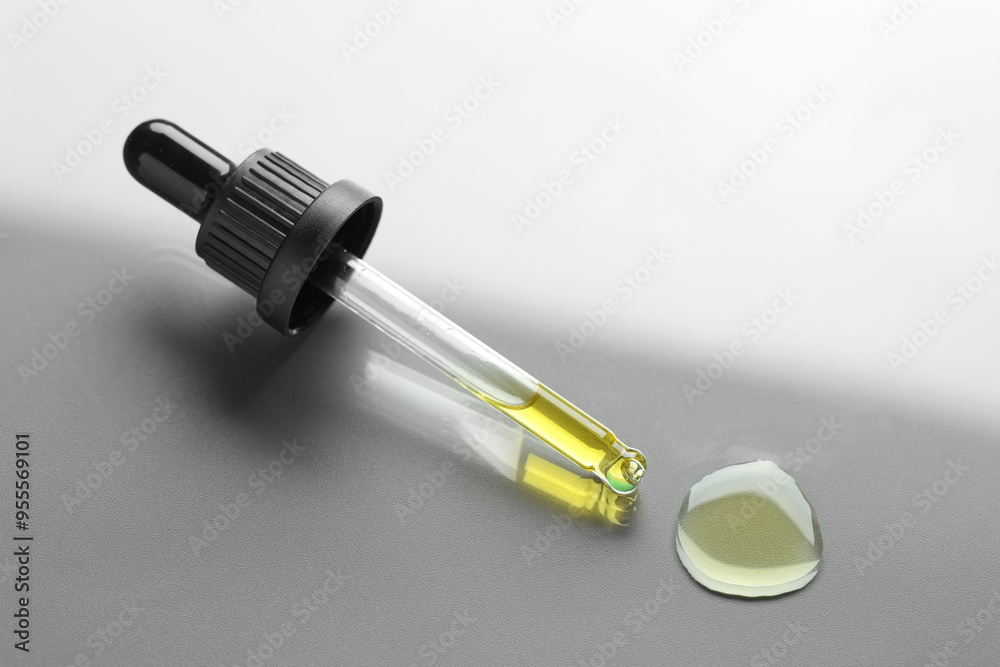 Dripping essential oil from pipette on grey background Dripping essential oil from pipette on grey background