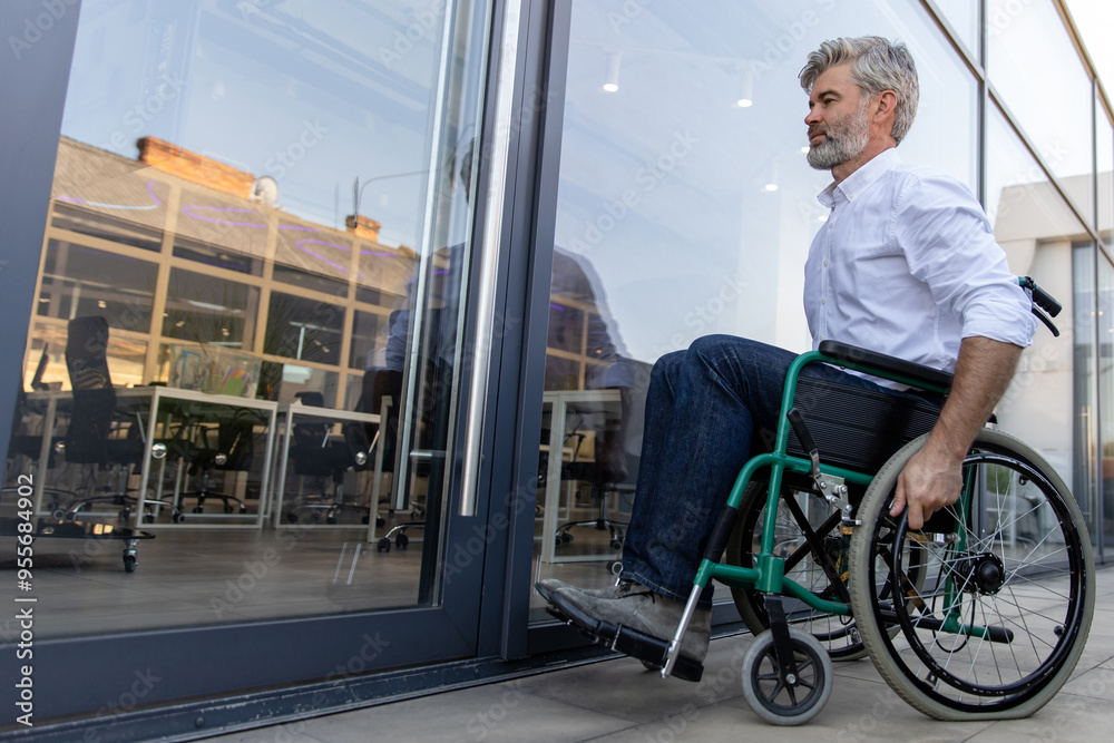 Gray-haired mature man on a wheelchair in the office area Gray-haired mature man on a wheelchair in the office area
