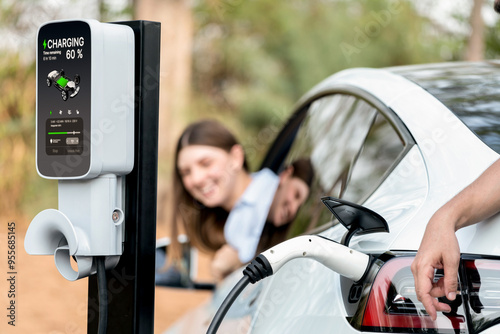 Lovely young couple recharging battery for electric car during autumnal road trip travel EV car in autumnal forest. Eco friendly travel on vacation during autumn. Exalt