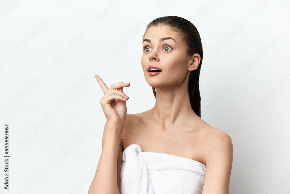 surprised young woman pointing upwards, with a towel wrapped around her, against a clean white background, expressing excitement or realization in a fresh and vibrant manner surprised young woman pointing upwards, with a towel wrapped around her, against a clean white background, expressing excitement or realization in a fresh and vibrant manner