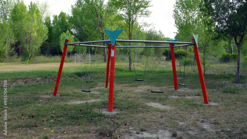 An empty playground features a large swing set with multiple swings, set in a peaceful park. Lush green trees surround the area, creating a calm atmosphere. An empty playground features a large swing set with multiple swings, set in a peaceful park. Lush green trees surround the area, creating a calm atmosphere.