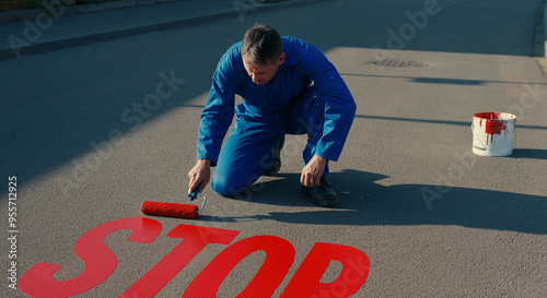 Man painting stop sign on road with red paint and roller for traffic safety measures photo