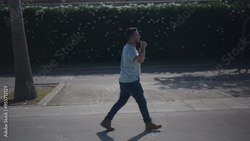 Young Caucasian boy walking from side to camera on the concrete walkway between palm trees cheering and applauding his favorite team photo