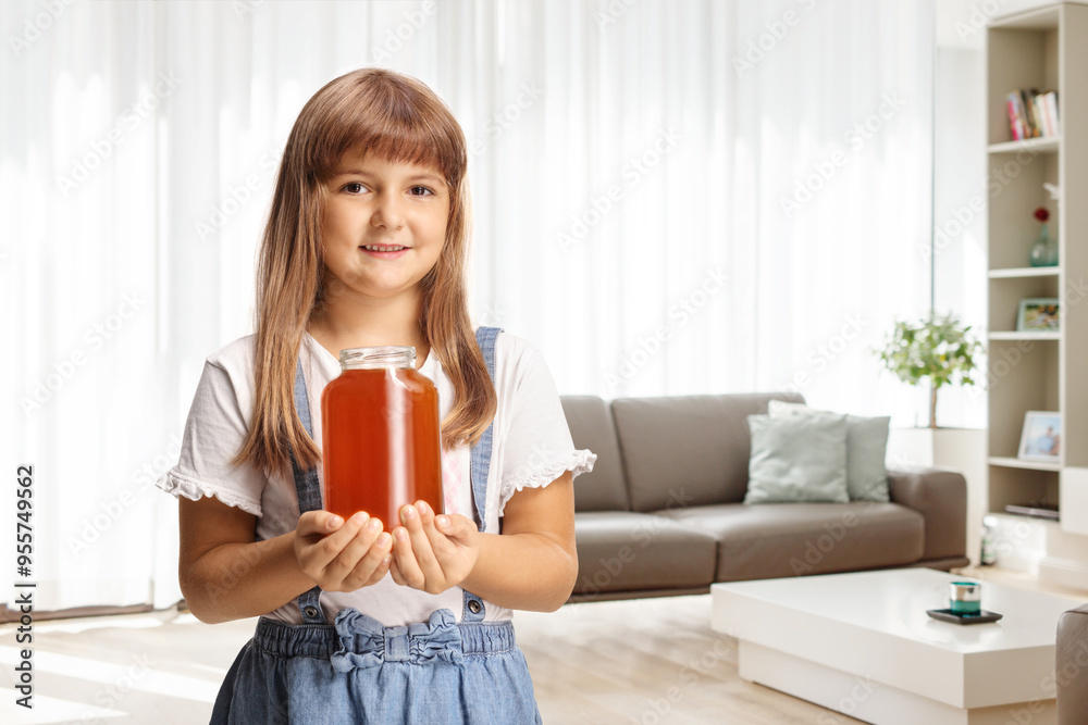 Happy little girl holding a honey jar and smiling at home Happy little girl holding a honey jar and smiling at home