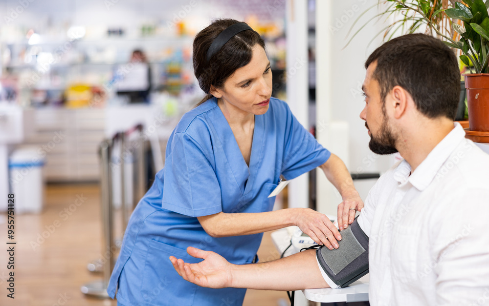 Fototapeta premium Nurce measuring man's blood pressure in drugstore. Diagnostic procedure in pharmacy.