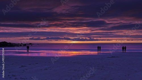  Midnight Sun time lapse. People on a sandy beach watching beautiful sunset over the ocean at Renowned Skagsanden Beach. Lofoten Islands, Northern Norway. 