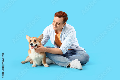 Redhead young happy man with cute Corgi dog sitting on blue background