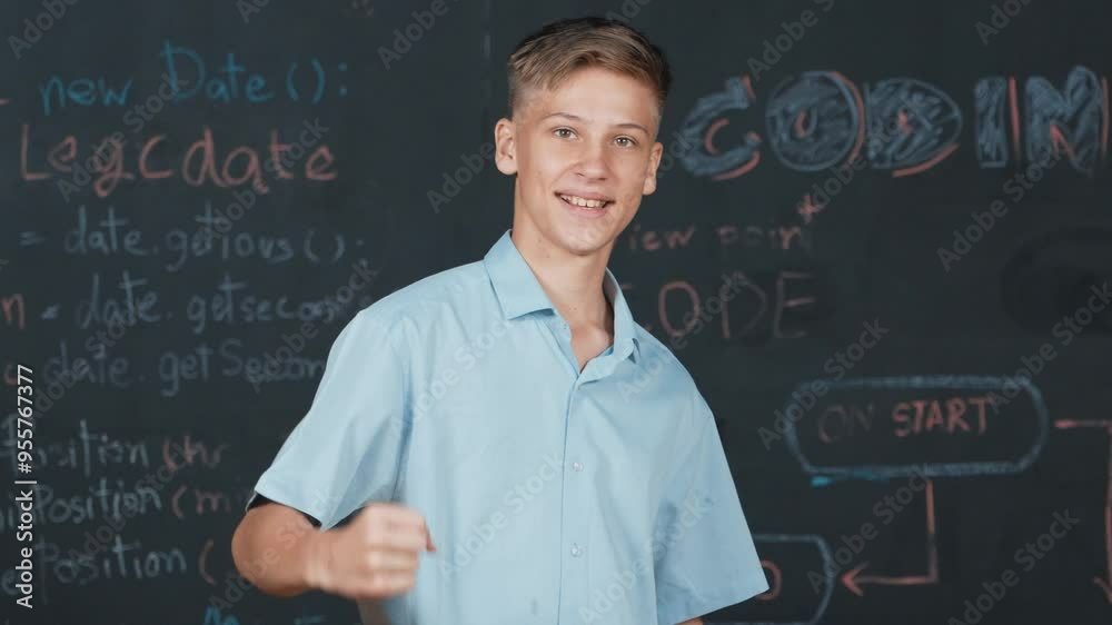 Handsome adult standing at blackboard with engineering code or prompt while attend in STEM class. Student raised hand to celebrate successful project or product while looking at camera. Edification Handsome adult standing at blackboard with engineering code or prompt while attend in STEM class. Student raised hand to celebrate successful project or product while looking at camera. Edification