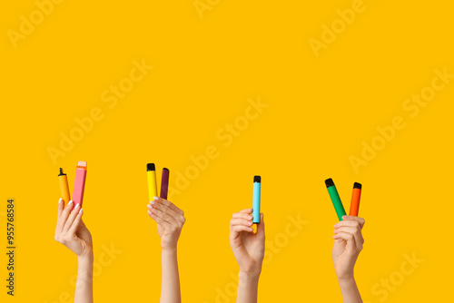 Many hands holding electronic cigarettes on yellow background