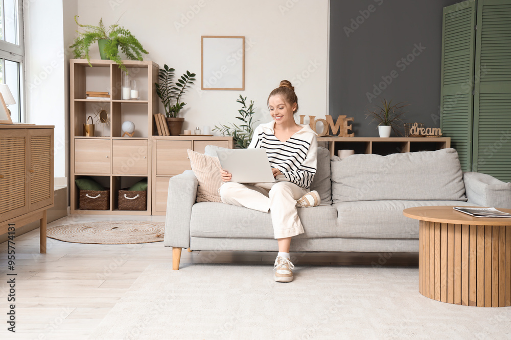 Obraz premium Young woman using modern laptop on sofa at home