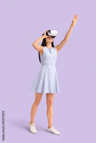 Young woman in VR glasses on lilac background