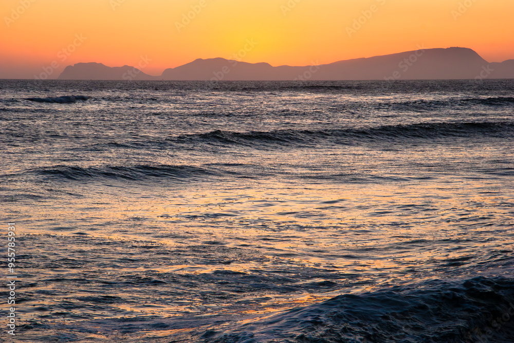 Sunset over calm ocean with distant mountain silhouettes Sunset over calm ocean with distant mountain silhouettes