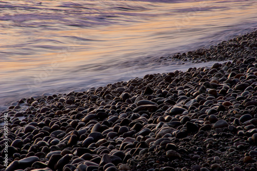 Fotografie Close-up of oceanside rocky beach with colorful sunset waves