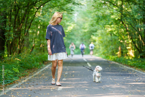 Girl walking the dog in the park forest. Rest concept. Woman walking with a dog on a leash in blue dress and with shoes.