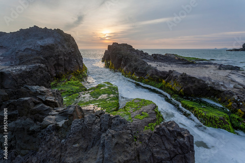 Sunset over mossy rocks and vibrant sea creating contrast