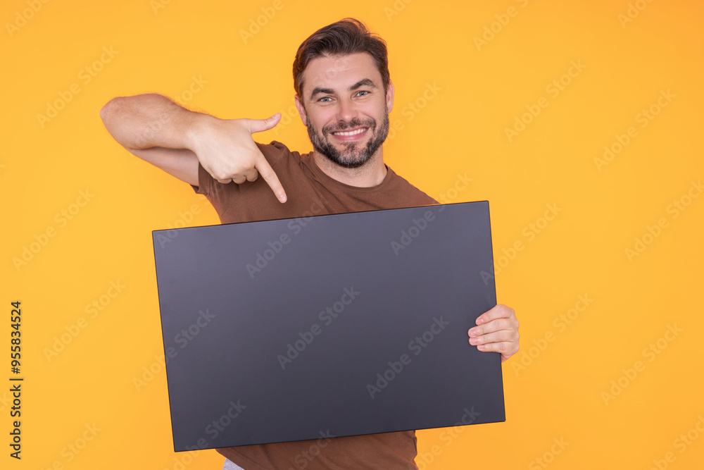 Happy man with blank banner isolated on studio background. Portrait of attractive man with empty blank poster. Man showing poster, pointing finger on signboard placard. Billboard or banner concept. Happy man with blank banner isolated on studio background. Portrait of attractive man with empty blank poster. Man showing poster, pointing finger on signboard placard. Billboard or banner concept.