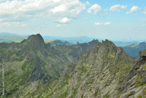 A series of high pointed mountain peaks with steep cliffs under a cloudy summer sky.