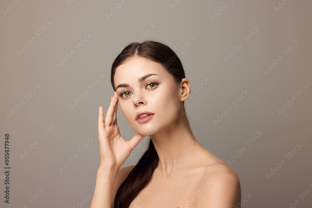 Beautiful young woman posing with hands on her face and looking at the camera on a gray background Beautiful young woman posing with hands on her face and looking at the camera on a gray background