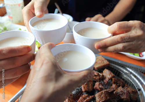 Four hands for toast with Makgeolli rice wine glass at Idong Galbi restaurant near Pocheon-si, South Korea photo