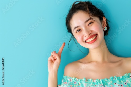 Radiant Japanese Woman in Off-Shoulder Dress Pointing Sideways with Grace, Studio Shot with Soft Blue Background and Natural Lighting, High-Resolution Professional Portrait