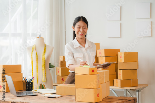 Smiling Business Owner: A young Asian woman, brimming with enthusiasm, stands amidst a mountain of packages in her home office. Her laptop, a tailor's dummy, and a notepad complete the scene, depictin photo