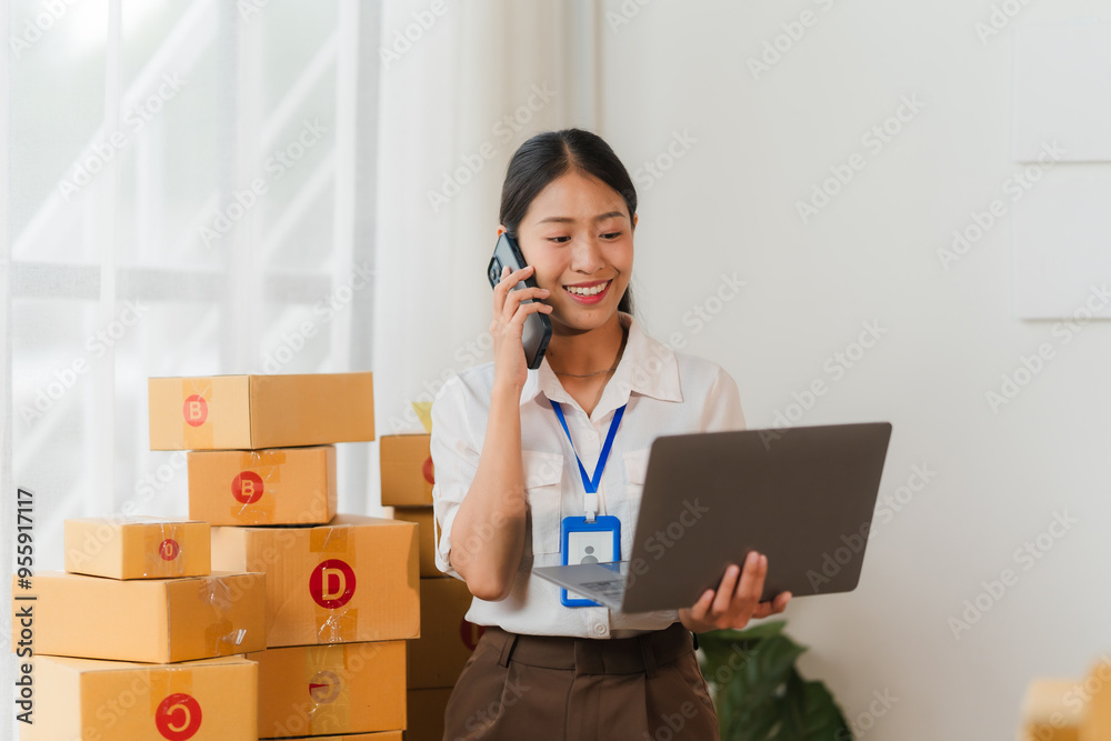 E-commerce Entrepreneur: Young Asian woman, surrounded by shipping boxes, manages orders and talks to customers on the phone, embodying the hustle of online business. E-commerce Entrepreneur: Young Asian woman, surrounded by shipping boxes, manages orders and talks to customers on the phone, embodying the hustle of online business.